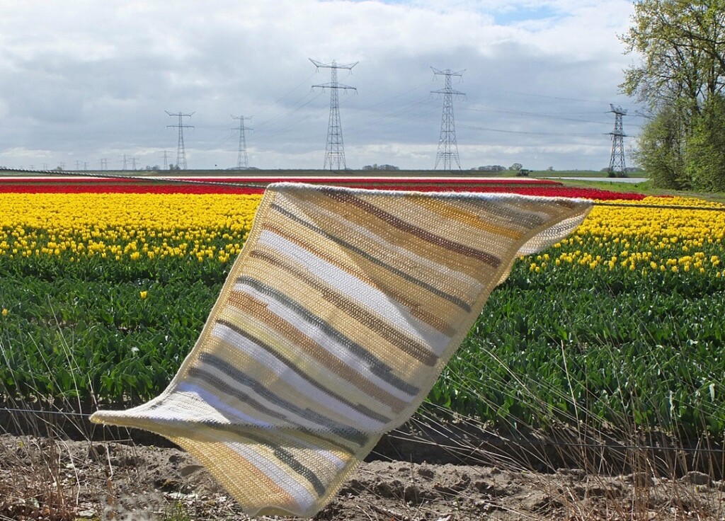 Beige gehaakte omslagdoek over hek bij bollenveld